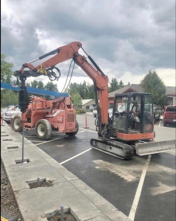 Excavator installing helical piers in a parking lot