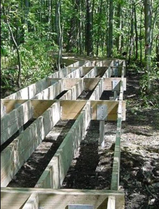 Elevated walkway framing on helical piers in a forest